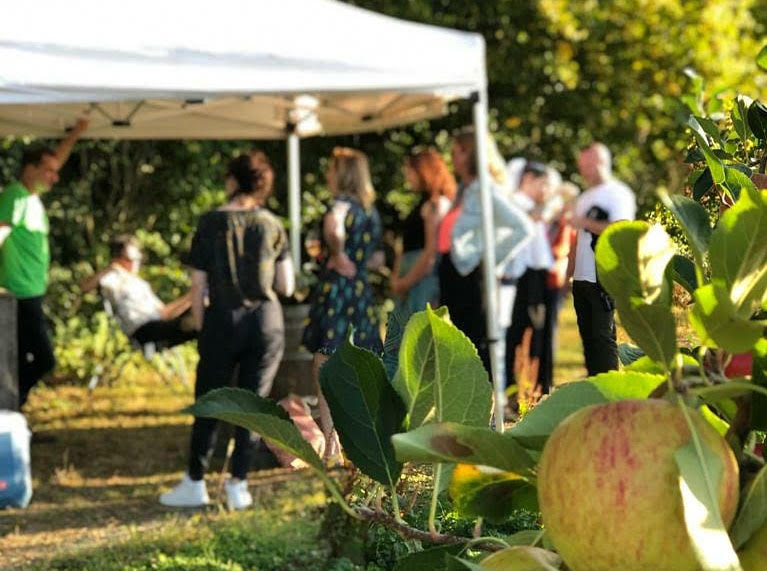Customers drinking wine at a marquee on a summer's day, slightly out of focus with an apple tree in the foreground.